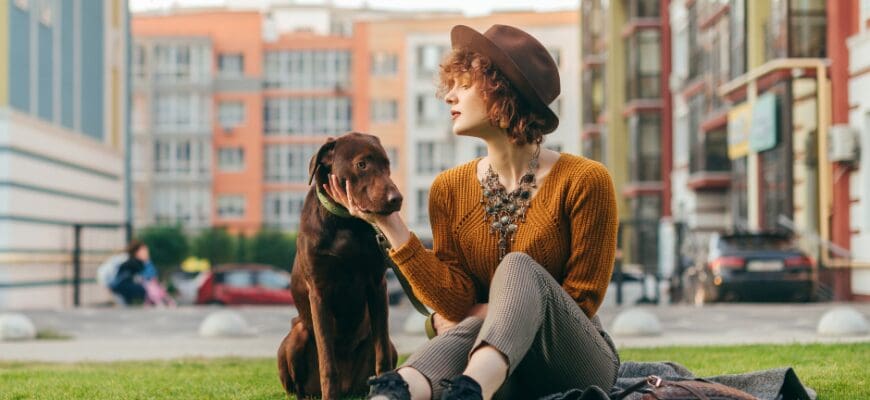 A woman sitting in an outdoor grass area with her dog